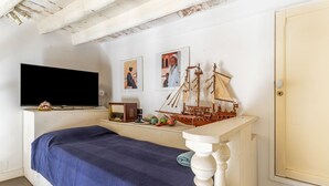 A room with a bed, a television, a model ship, and framed pictures on the wall. - GuestHost - House Overlooking the Harbour (Trani)