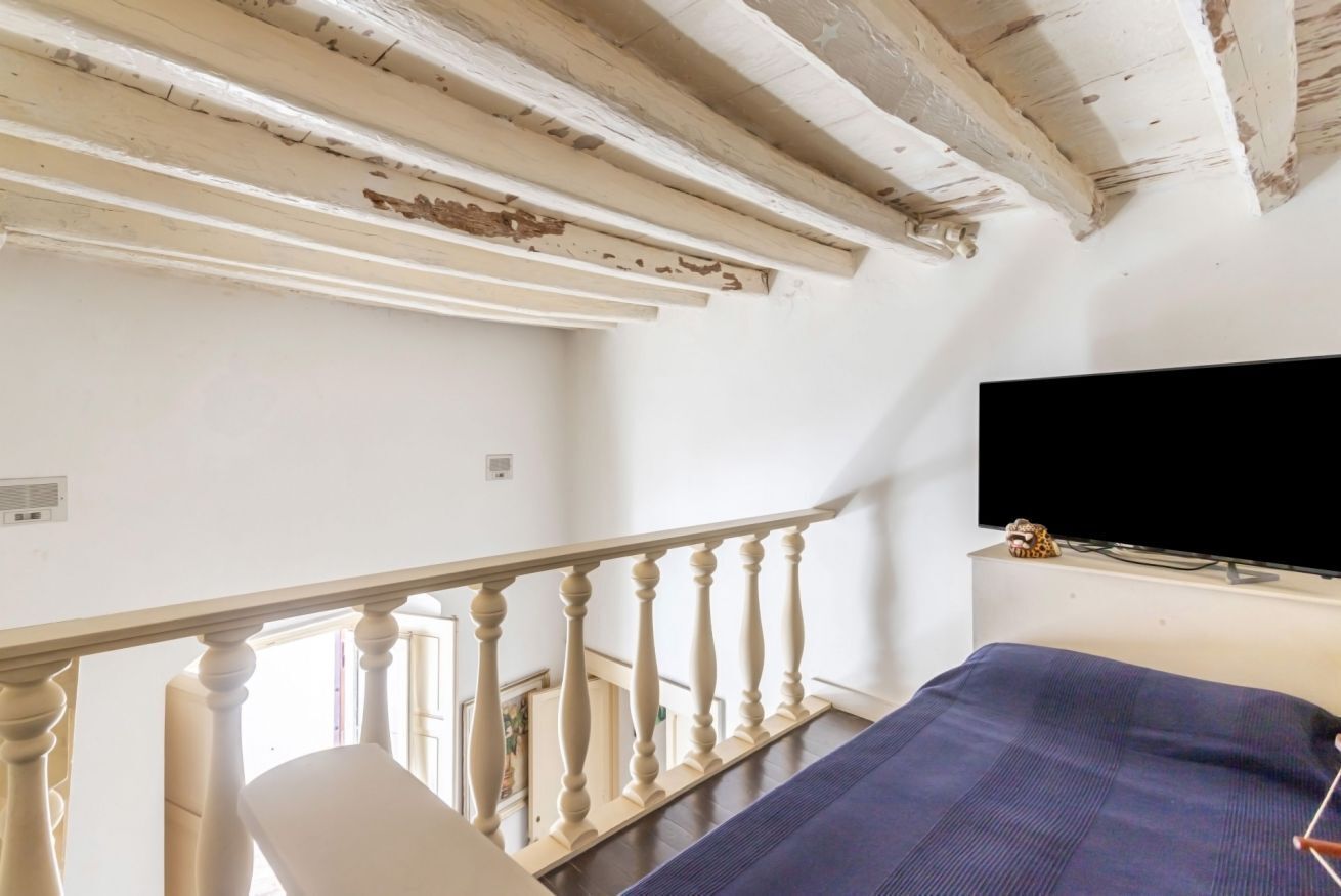 A room with a bed, a television, and a balcony with a railing.