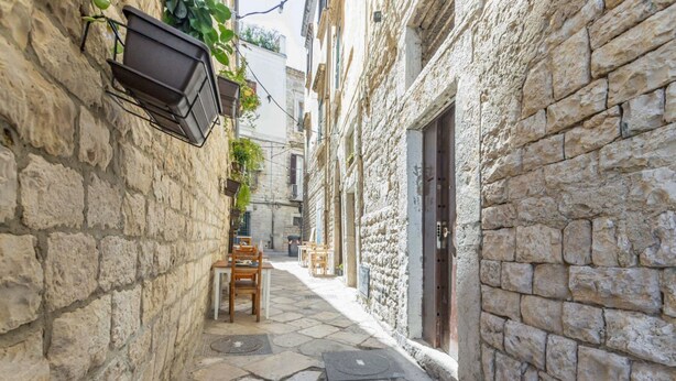 A narrow stone alley with a table and chairs set up for outdoor dining, flanked by buildings with stone walls and a door. - GuestHost - House Overlooking the Harbour (Trani)