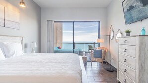 A hotel room with a large bed, a desk with a chair, a dresser, and a view of the ocean through a large window. - Las Palomas Phase II Cabrillo 1506 Exceptional Oceanview 2BR 2BA Unit (Puerto Peñasco)