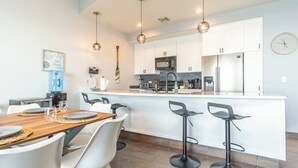 A modern kitchen with white cabinets, a central island with bar stools, a microwave, and a refrigerator. - Las Palomas Phase II Cabrillo 1506 Exceptional Oceanview 2BR 2BA Unit (Puerto Peñasco)