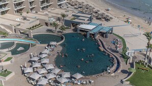 Un complexe hôtelier doté d’une piscine centrale, de nombreuses chaises longues et d’un espace plage.
