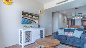 Un salon comprenant un canapé, une table basse, un meuble et un tableau représentant une piscine.