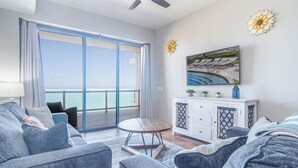 Un salon moderne doté d’une grande porte-fenêtre coulissante donnant sur un balcon avec vue sur la mer. On y trouve un canapé, une petite table ronde et un meuble contenant des objets décoratifs.