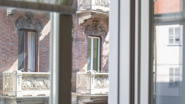Une vue à travers la fenêtre d’un bâtiment doté de balcons richement décorés et d’une façade en briques.