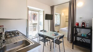 Une cuisine compacte équipée d’une cuisinière à gaz, d’une table à manger avec des chaises, d’un téléviseur fixé au mur et d’un lit donnant sur une fenêtre.