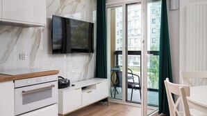 A modern kitchen with a marble backsplash, a flat-screen TV, and a dining area with a table and chairs. - Bemowo Narwik Deluxe Studio (Warszawa)