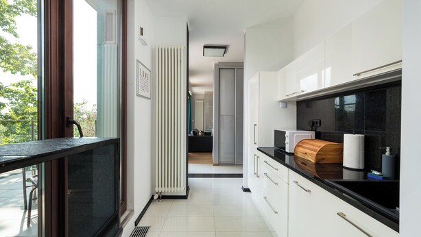 A modern kitchen with white cabinets, a black countertop, and a view to the outside.