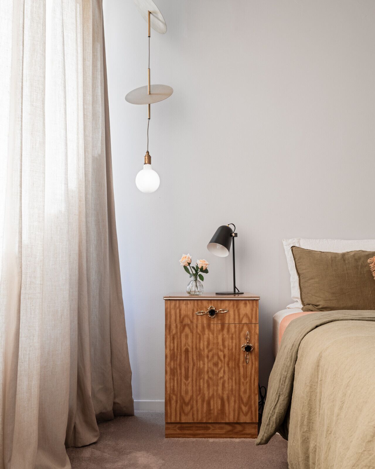 Et soveværelse med seng, sengebord, lampe og gardiner.