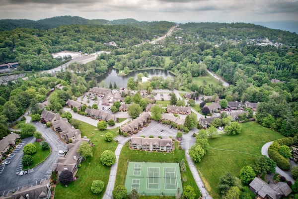 The full Chetola campus from above, with tennis courts, a shimmering pond, and lush Blue Ridge forests stretching to the horizon.