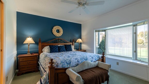 A bedroom with a bed, two bedside tables, a nightstand, a bench, a ceiling fan, and a window with blinds. - Chetola: Holly 4 - Condo near Downtown Blowing Rock! (Blowing Rock)