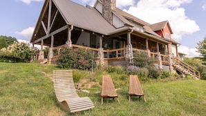 A large house with a stone chimney, a wooden deck, and a stone staircase leading to the entrance. - Robin Hoods Retreat - Luxury home, walk to river, hot tub, fire pit! (Jefferson)