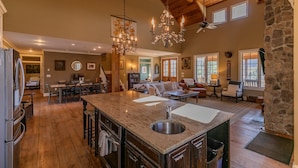 A spacious kitchen with a large island, wooden flooring, and a stone accent wall. - Robin Hoods Retreat - Luxury home, walk to river, hot tub, fire pit! (Jefferson)