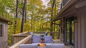 A deck with outdoor seating and a fire feature, surrounded by trees.