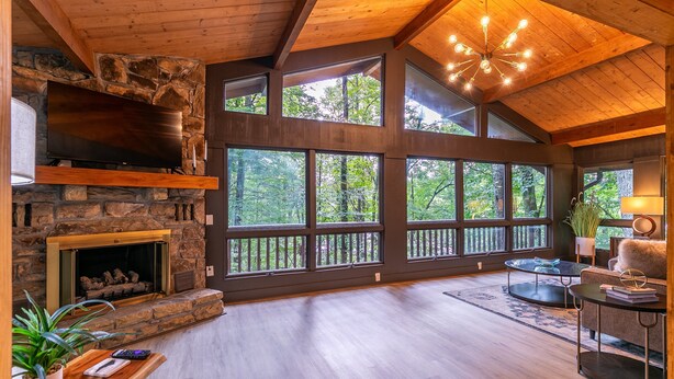 A spacious living room with a stone fireplace, large windows, and a wooden ceiling.