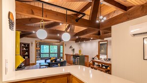 A kitchen with wooden beams, a white countertop, and a dining area with a view of the outdoors.