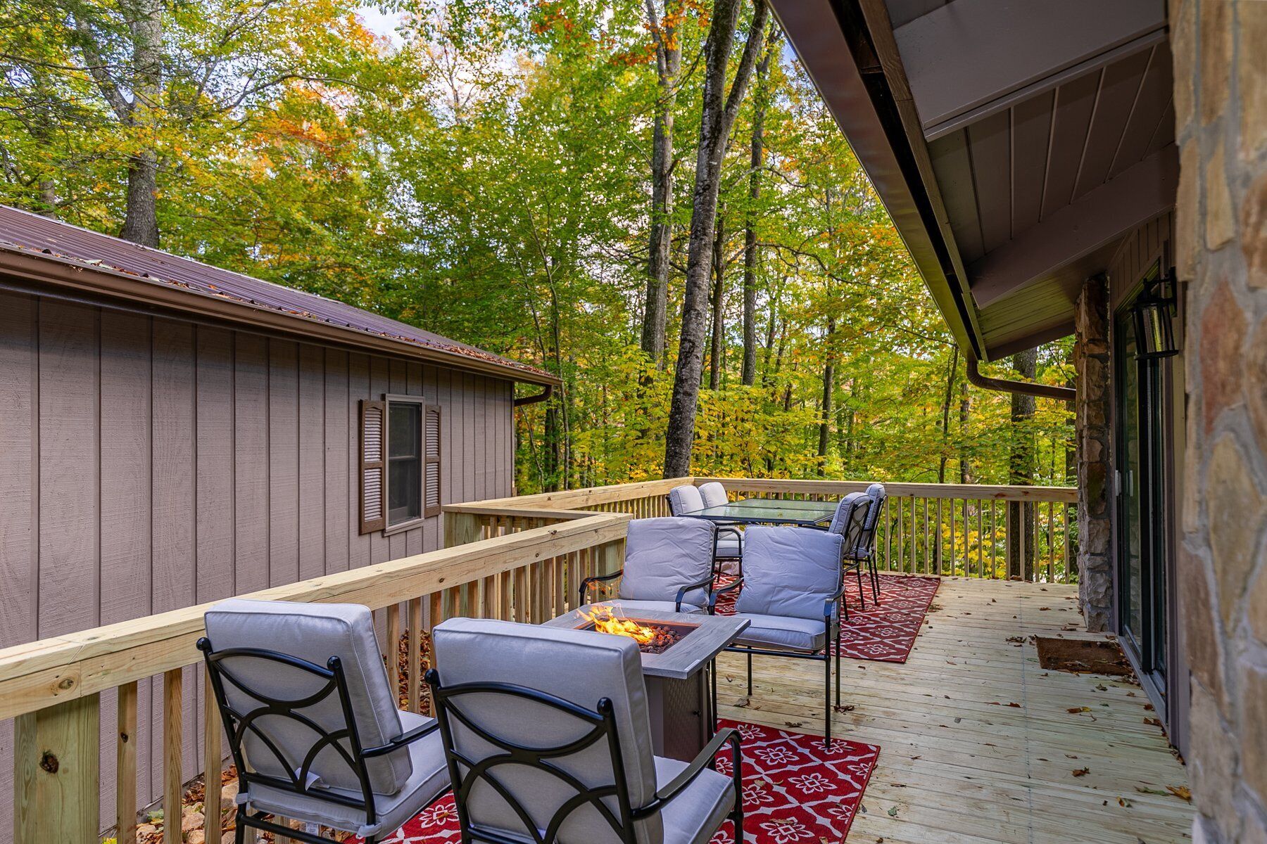 A wooden deck with outdoor seating, a fire pit, and a view of a forested area.