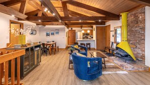 A spacious living area with wooden beams, a fireplace, and a kitchen in the background.