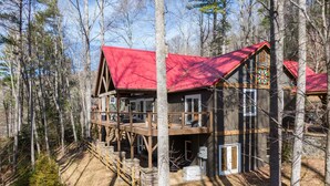 Uma cabana com telhado vermelho, deck de madeira e uma janela grande.
