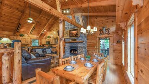 Ein Blockhaus-Interieur mit Kamin aus Stein, einem Holztisch und einer gemütlichen Sitzecke.