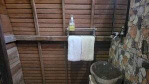 A rustic bathroom with a wooden slatted wall, a stone sink, and a towel hanging on a rack. - Jambu Guest House  (Penida Island)
