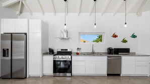A modern kitchen with white cabinets, stainless steel appliances, and a window with a view of greenery.