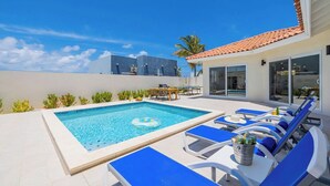 A pool area with a clear blue pool, lounge chairs, and a small table with a bucket.