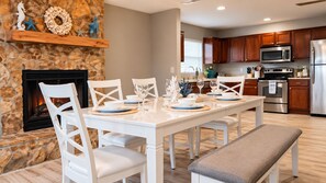 A dining area with a stone fireplace, white chairs, and a wooden table set for four. - Beach Days & Sunshine Near IMG & Anna Maria (Bradenton)