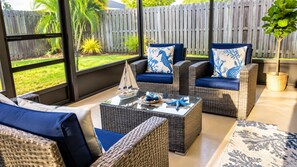 A sunlit patio with wicker furniture, a glass coffee table, and decorative pillows. - Beach Days & Sunshine Near IMG & Anna Maria (Bradenton)