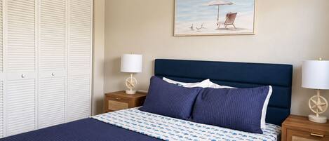 Quarto com cama, duas mesas de cabeceira, cabeceira, um quadro e um guarda-roupa.