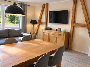 Una sala moderna con una mesa de comedor de madera, un sofá gris y un televisor montado en una pared de madera.