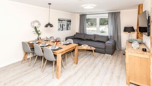 Una sala de estar moderna con comedor, un sofá gris, una mesa de comedor de madera y un televisor montado en la pared.