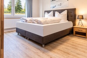 Un dormitorio moderno con una cama grande, una mesita de noche y una ventana con vistas a árboles.