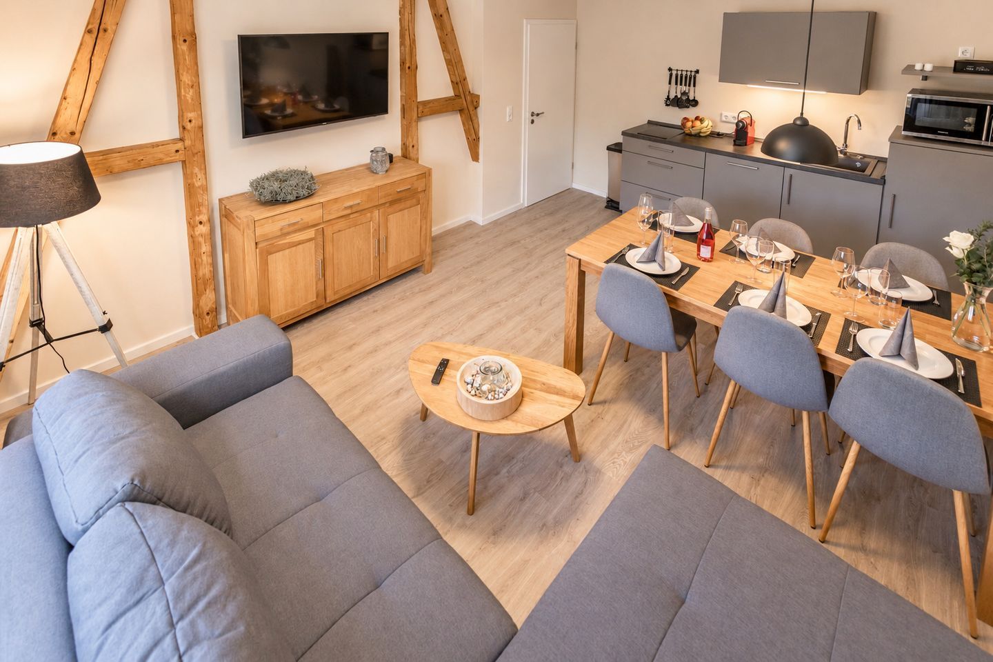 A modern living room with a sofa, a dining table set for four, and a kitchen area with a microwave and sink.