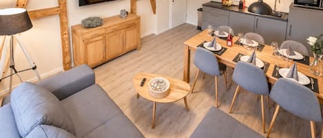 A modern living room with a sofa, a dining table set for four, and a kitchen area with a microwave and sink.