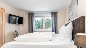 Habitación de hotel con cama, televisión de pantalla plana, ventana con cortinas y un cuadro en la pared.