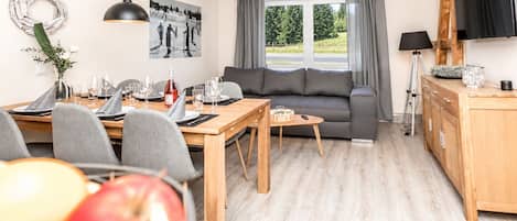 Ett modernt vardagsrum med en soffa, ett matbord med stolar och en tv som är monterad på väggen.