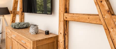 A room with a wooden cabinet, a flat-screen TV mounted on a wall, and exposed wooden beams.