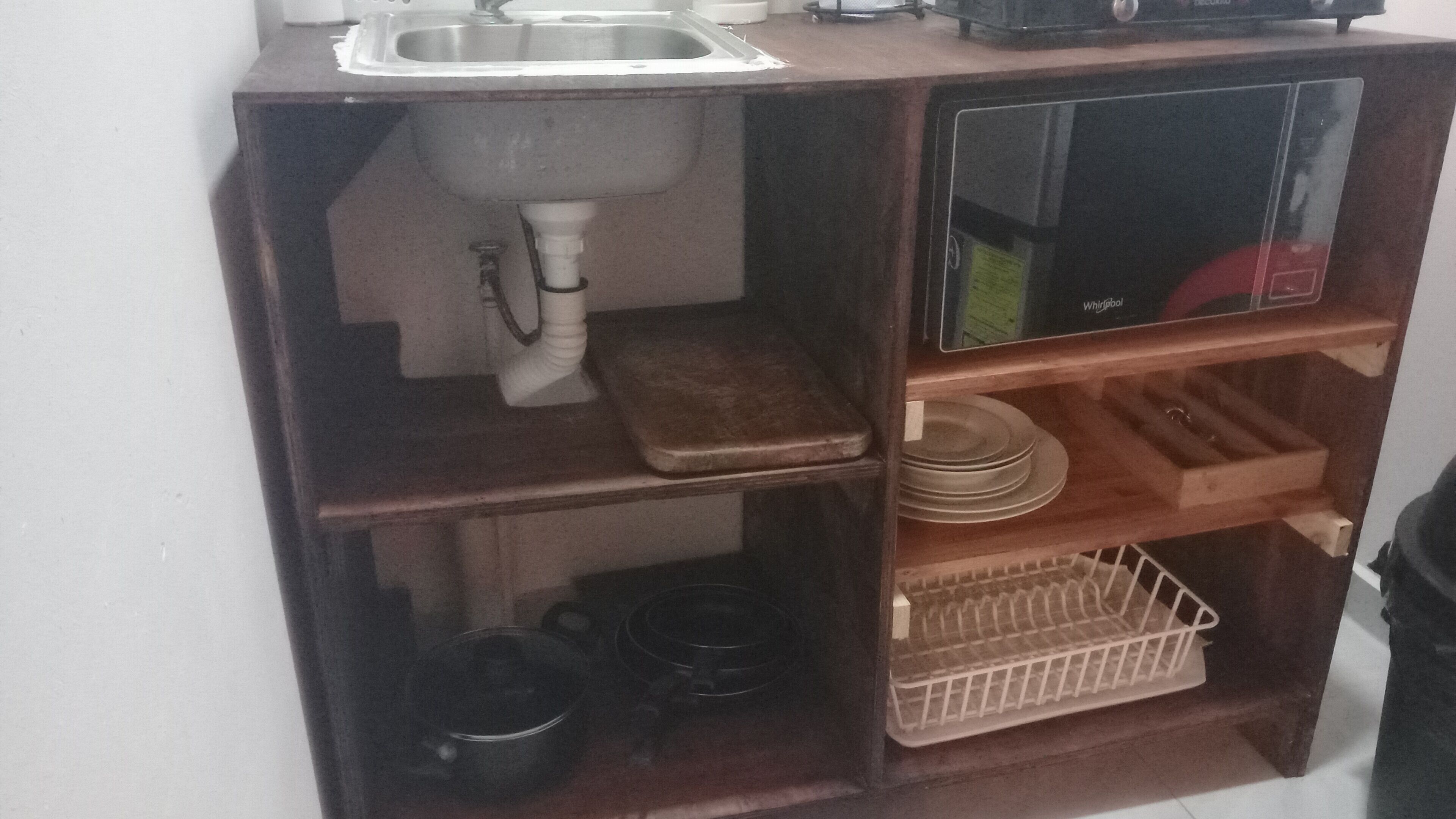 A kitchen with a sink, a microwave, and shelves with dishes and cookware.