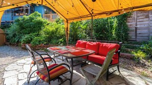An outdoor patio with a yellow canopy, red cushioned seating, and a table with metal chairs. - Capitol Hill House - Spacious, Cheery, Sun-filled (Seattle)