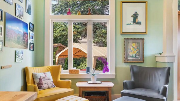 A cozy living room with a yellow armchair, a grey armchair, and a small table with a vase of flowers. - Capitol Hill House - Spacious, Cheery, Sun-filled (Seattle)