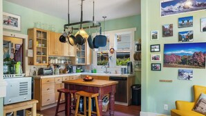 A kitchen with wooden cabinets, a central island, hanging pots, and a dining area with stools. - Capitol Hill House - Spacious, Cheery, Sun-filled (Seattle)