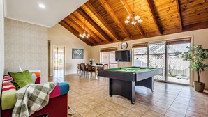 Un salon spacieux avec une table de billard, un canapé rouge et un coin repas comprenant des chaises et une table.