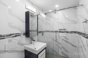 A modern bathroom with a glass shower enclosure, a white sink, and a dark cabinet.