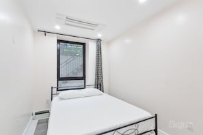 A small, clean room with a bed, a window with a view, and an air conditioning unit.