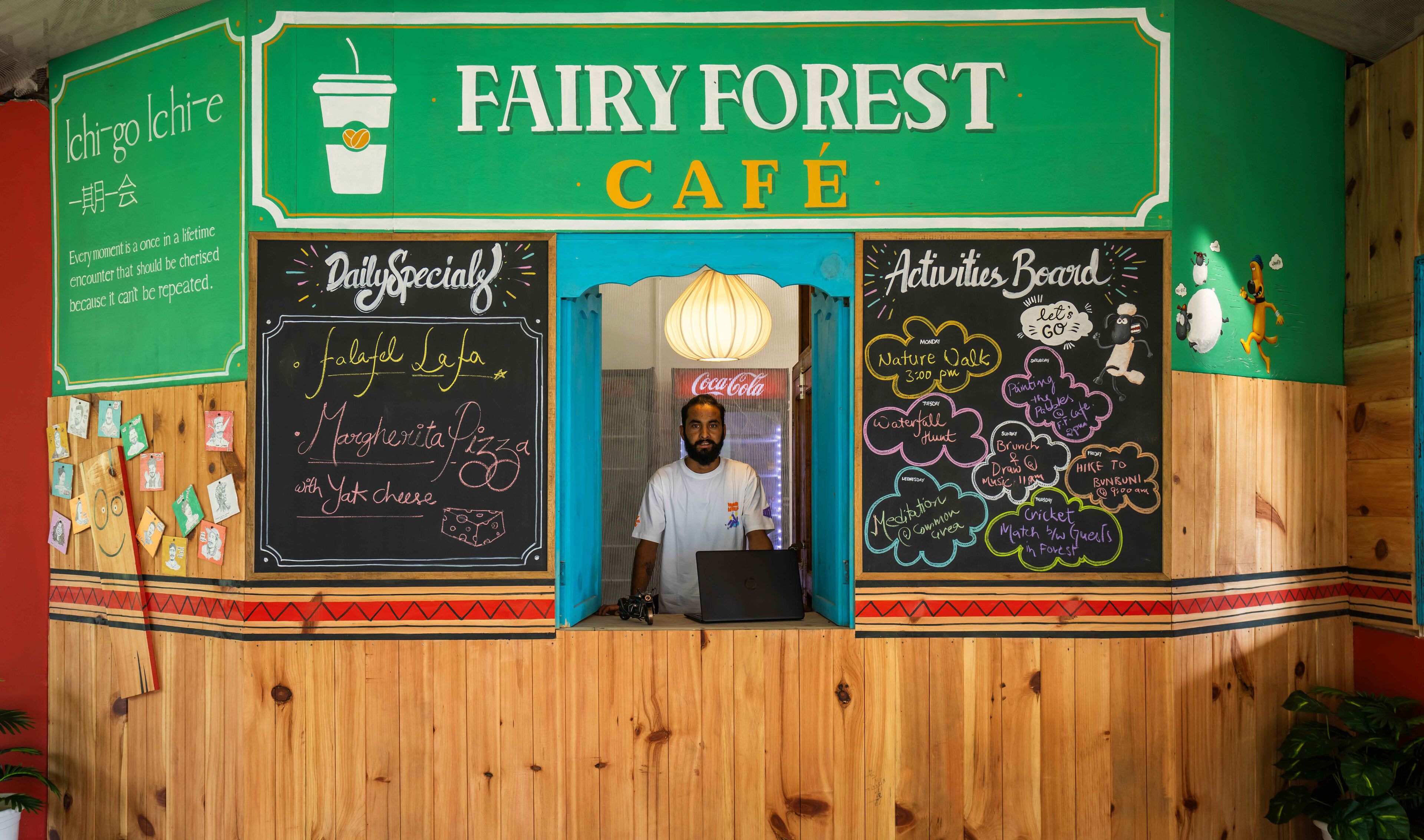 Una cafetería llamada 'FAIRY FOREST CAFE' con un menú en una pizarra, un tablón de anuncios y un cartel con una cita.