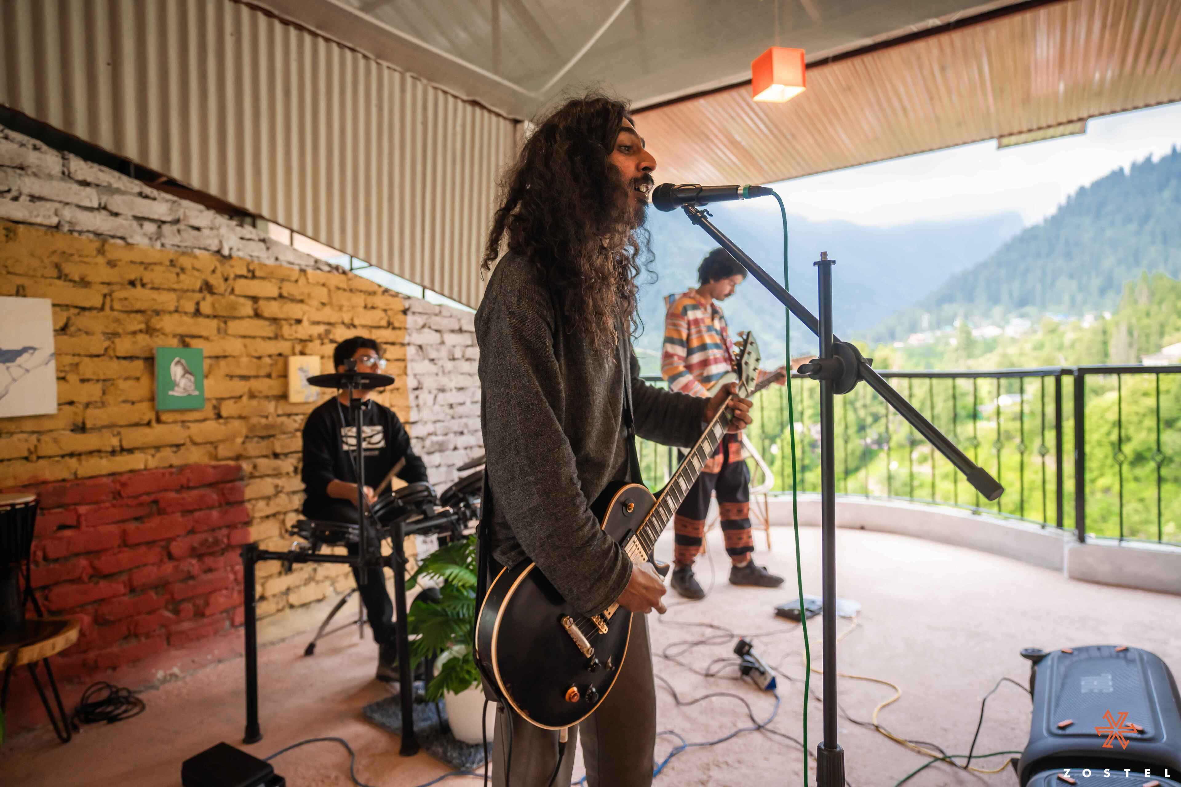 A musician performing on a stage with a mountainous backdrop, a brick wall, and a railing overlooking the scenery.