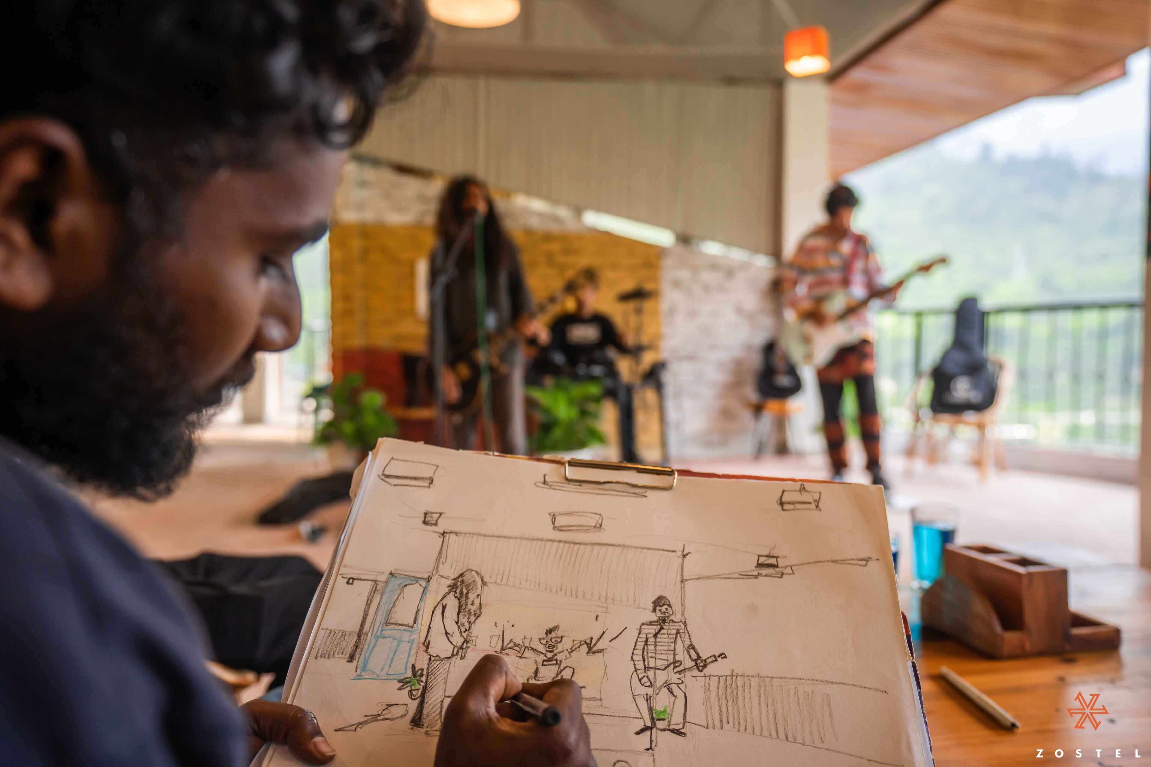 A person holding a sketchbook with a drawing of a band performing in a room with a wooden ceiling and large windows.