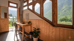 A wooden room with a dining table, chairs, a potted plant, and large windows offering a mountain view. - Zostel Pulga (Bhuntar)
