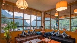 A cozy room with a large window, a sofa, a table, and a potted plant. - Zostel Pulga (Bhuntar)